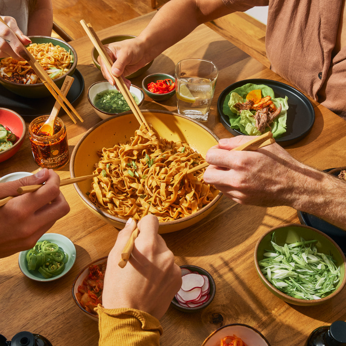 five people enjoying a bowl of momofuku noodles and original chili crunch jar w/ momofuku chopsticks 