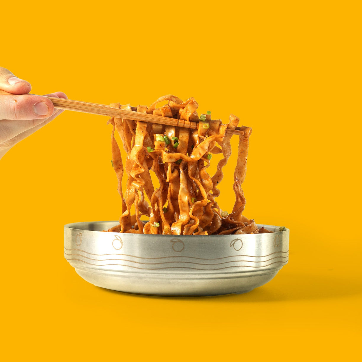 Momofuku Noodle bowl with chopsticks pulling noodles on orange background