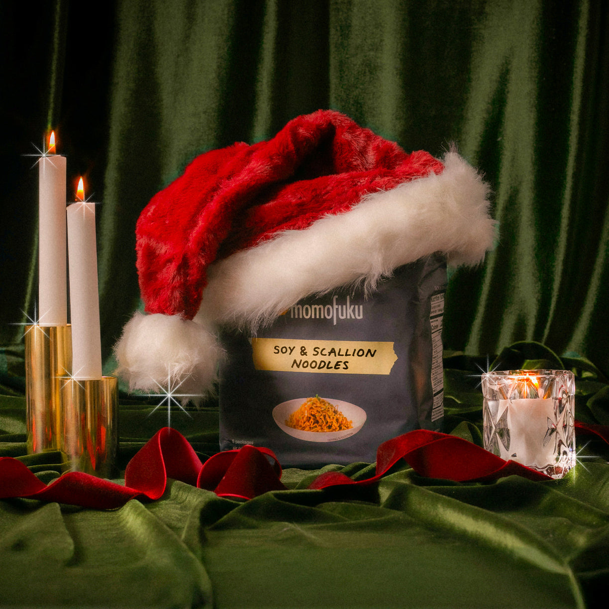 festive display of a bag of Soy & Scallion noodles with Santa hat on top with velvet green background